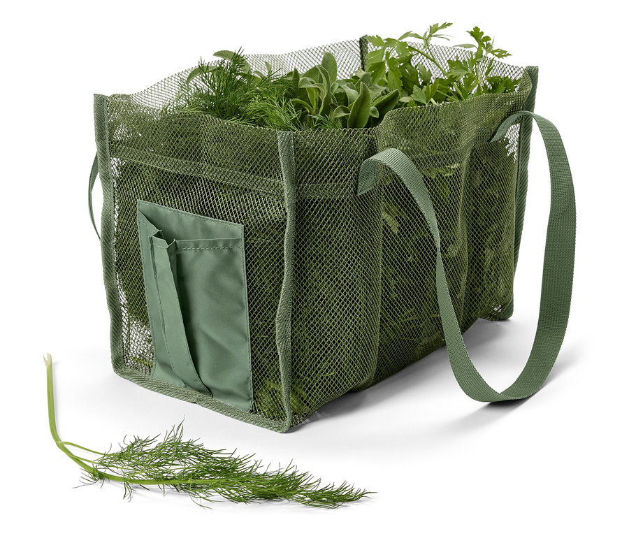 Eine grüne Netzstofftasche ist mit frischen Kräutern gefüllt, darunter Dill, Salbei und Petersilie. Ein Dillstängel liegt davor.