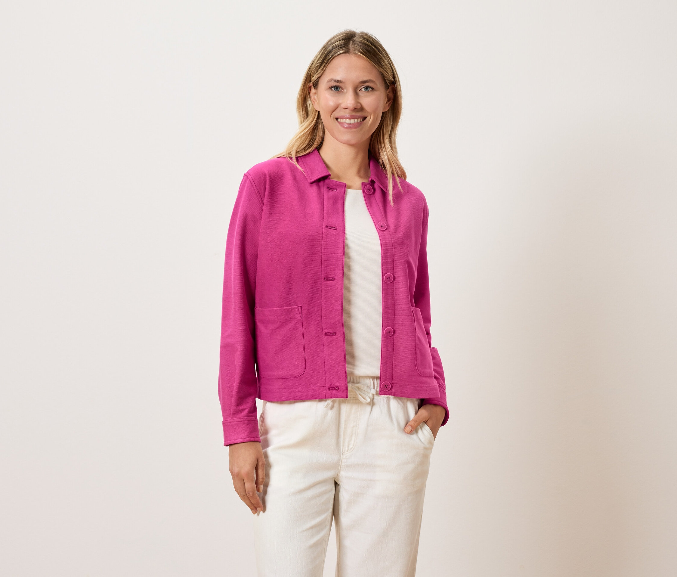 Frau trägt eine pinke Jacke über einem weißen Oberteil und cremefarbene Hosen.