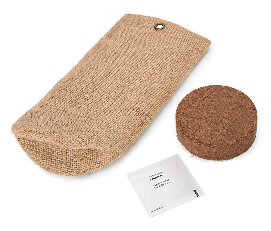 Eine braune Jutetüte liegt neben einer runden, braunen Tablette und einer kleinen weißen Packung.