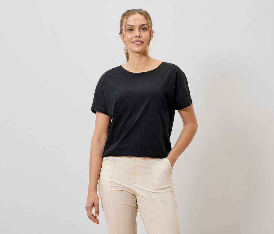 Frau mit schwarzem T-Shirt und beigen Hosen, die in die Kamera lächelt.