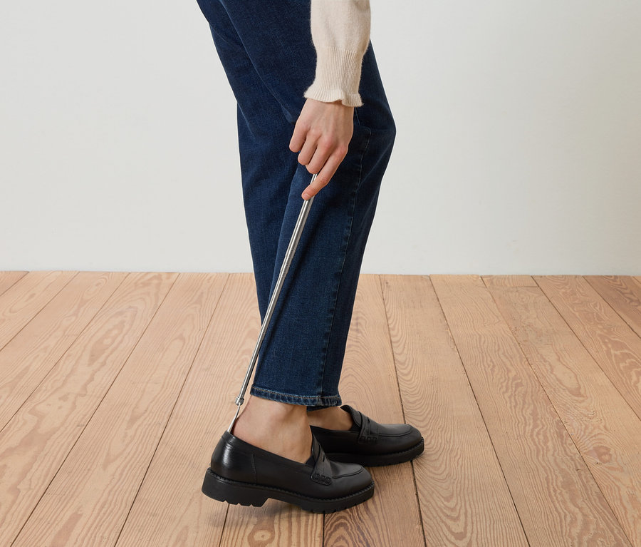 Person, die mit einem Schuhlöffel schwarze Slipper anzieht.