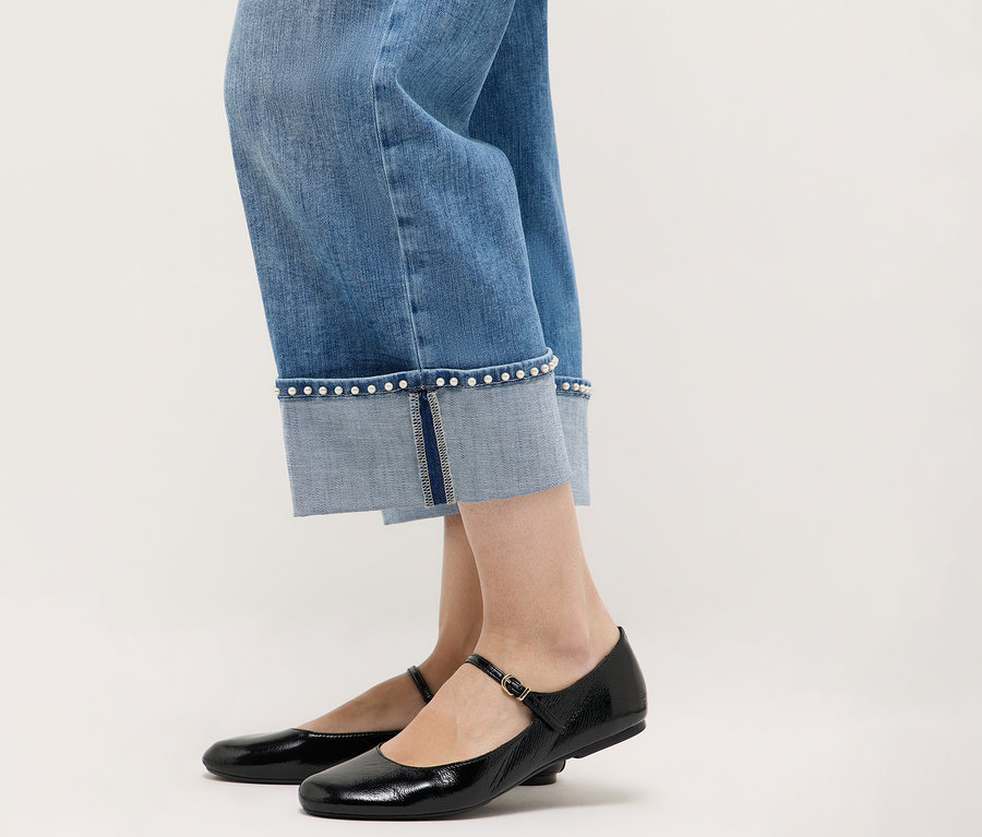 Nahaufnahme von Beinen in Angels Denim »Linn Cool« Jeans, kombiniert mit schwarzen Mary Jane Schuhen vor einem neutralen Hintergrund.