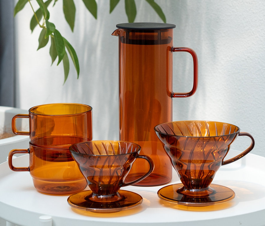 Auf einem Tisch steht ein HARIO »Colors« Tee- und Kaffee-Set in Amber. Das Set beinhaltet zwei Tassen, zwei Filterhalter und einen Krug.