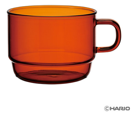 Eine bernsteinfarbene, transparente Tasse mit Henkel steht vor einem weißen Hintergrund.