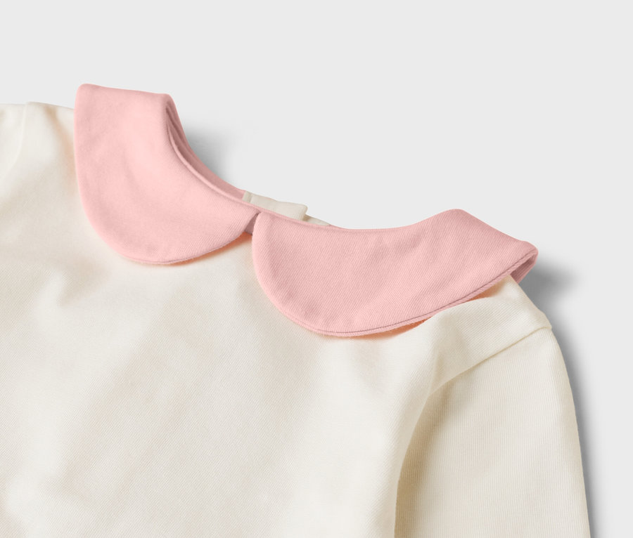Detailansicht eines cremefarbenen Oberteils mit einem rosa Bubikragen.