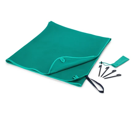 Ein türkisfarbenes Handtuch liegt teilweise gefaltet neben einer kleinen Tasche und Heringen auf einem weißen Hintergrund.