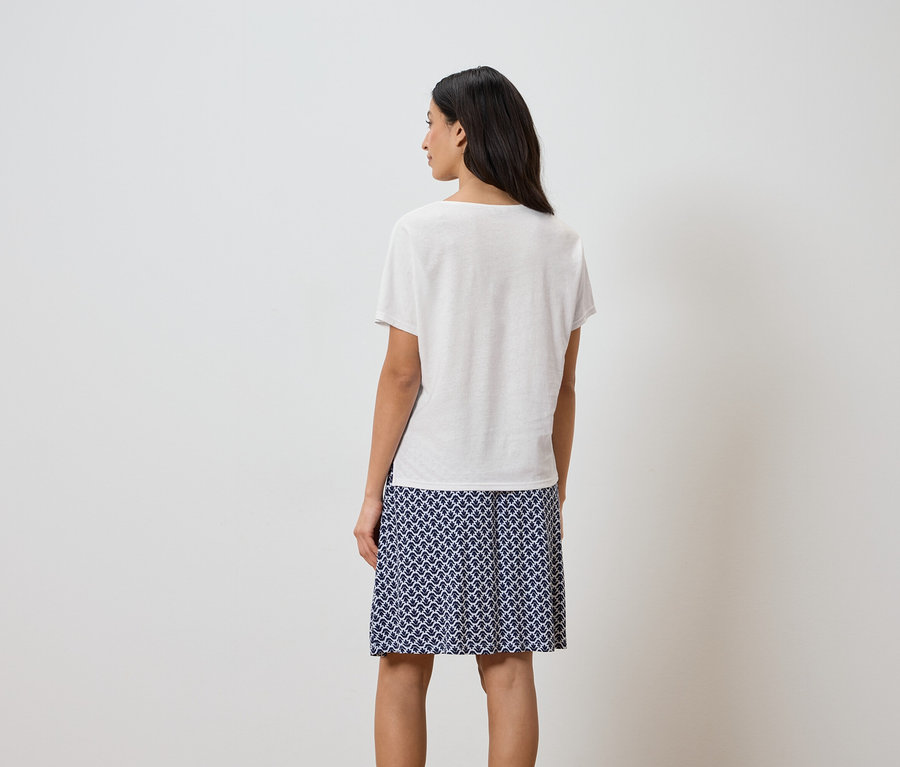 Rückansicht einer Frau mit dunklen Haaren, die ein weißes T-Shirt und einen Rock mit blauem Muster trägt.