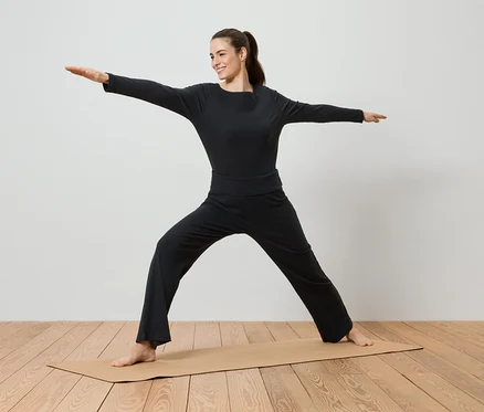 Eine Frau in schwarzer Sportbekleidung macht Yoga auf einer Yogamatte.