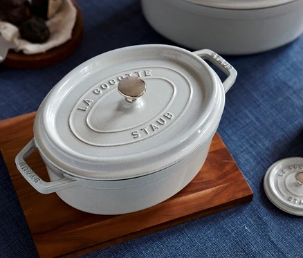 Ein weißer STAUB Bräter »Cocotte 29« (ca. 4,2 l) steht auf einem Holzbrett. Im Hintergrund ist ein weiterer weißer STAUB Bräter »Cocotte 33« (ca. 6,7 l) zu sehen.
