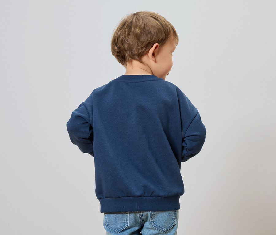 Ein Kind mit blonden Haaren trägt ein marineblaues Sweatshirt und Jeans.