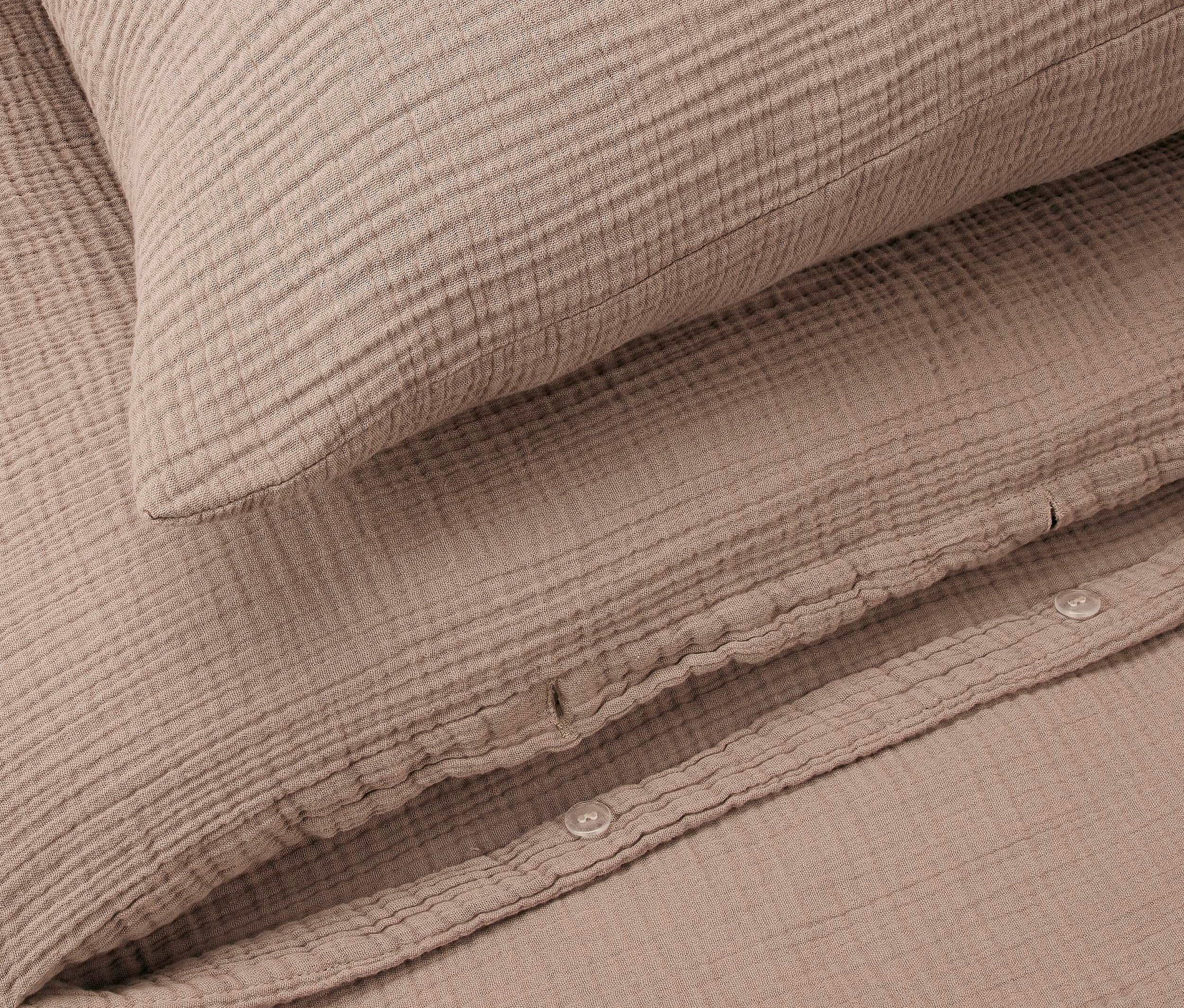 Nahaufnahme eines beigen Kopfkissens auf einem gleichfarbigen Bettbezug.