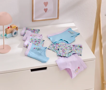 Auf einem weißen Tisch liegen mehrere Mädchenslips in Lila und Hellblau mit Blumenmuster.