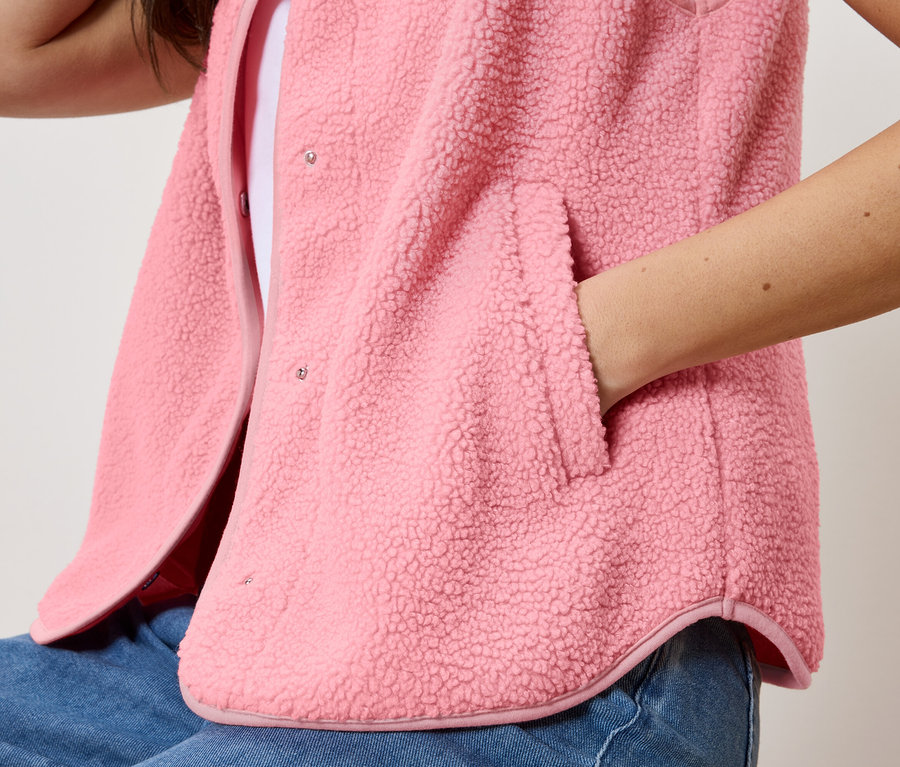 Frau mit Hand in der Tasche der Teddy-Weste über einem weißen Top und Jeans.