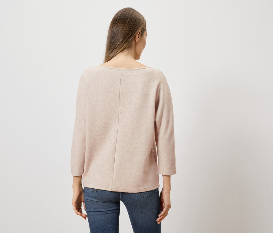 Rückansicht einer Frau mit langen braunen Haaren, die einen hellrosa Pullover und blaue Jeans vor einem weißen Hintergrund trägt.