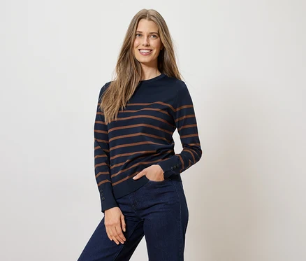 Frau mit einem dunkelblauen, gestreiften Pullover und Jeans, eine Hand in der Hosentasche.