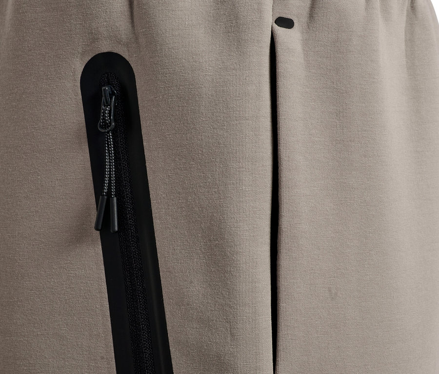 Nahaufnahme einer beigen Jogginghose mit einer schwarzen Reißverschlusstasche und einer offenen Tasche.