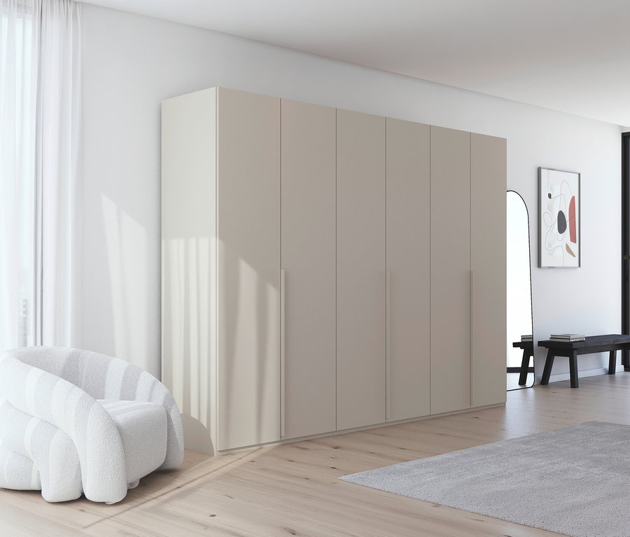 Ein helles Zimmer mit einem großen, beigen Kleiderschrank, einem weißen Sessel und einem grauen Teppich auf hellem Holzboden.