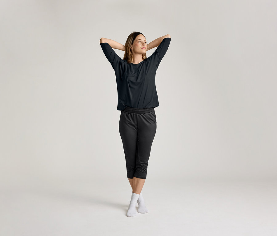 Frau mit verschränkten Händen hinter dem Kopf trägt ein schwarzes 3/4-Sportshirt.