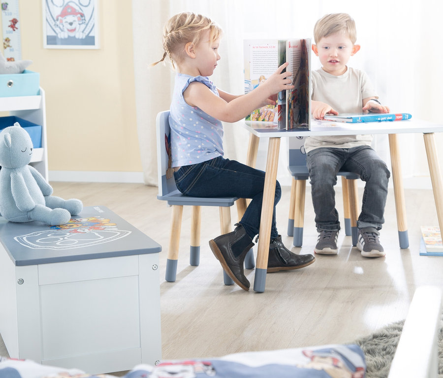 Ein Mädchen und ein Junge sitzen an einem Tisch und lesen ein Buch.
