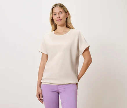 Frau trägt ein helles T-Shirt und lila Hosen.