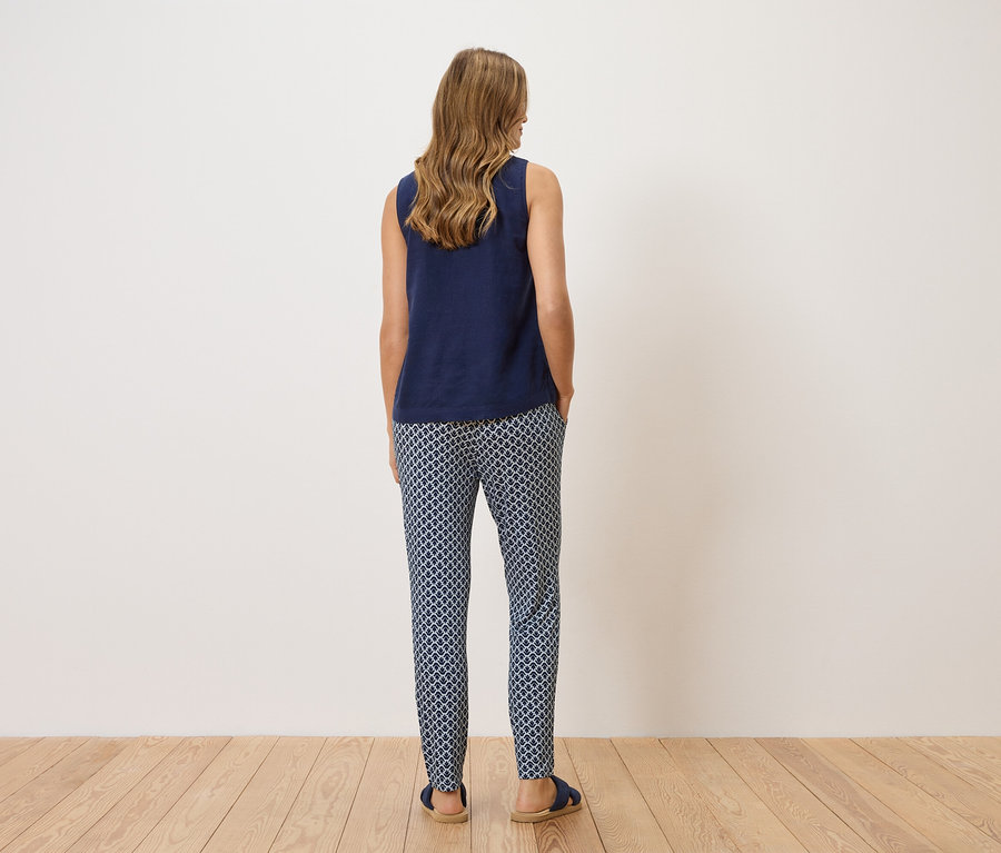 Eine Frau steht mit dem Rücken zur Kamera und trägt ein marineblaues Top und gemusterte Hosen.