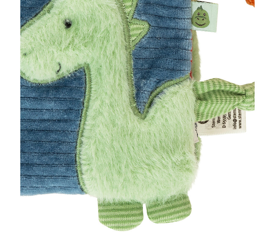 Nahaufnahme einer hellgrünen, flauschigen Dinosaurier-Applikation auf blauem Rippstoff. Der Dinosaurier hat kleine schwarze Augen, ein gesticktes Lächeln und gestreifte grün-weiße Füße. Ein kleines Etikett mit einem grünen Dinosaurierkopf ist sichtbar.
