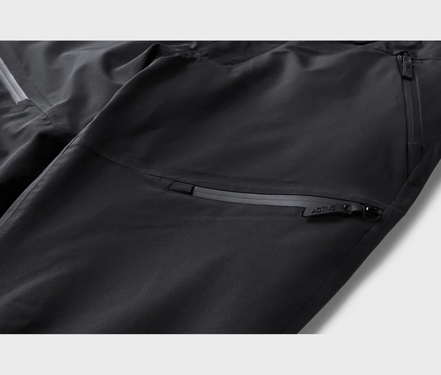 Nahaufnahme einer schwarzen Hose mit Reißverschlusstaschen und einem reflektierenden Streifen. Ein Reißverschlussanhänger ist mit "ACTIVE" beschriftet.