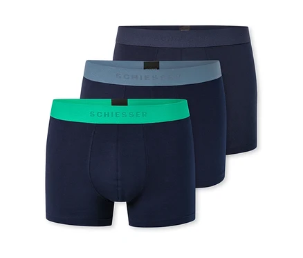 Drei dunkelblaue Herren-Boxershorts sind diagonal gestapelt. Die vorderste hat einen leuchtend grünen Bund, die mittlere einen graublauen und die hinterste einen dunkelblauen Bund, alle mit "SCHIESSER"-Schriftzug.