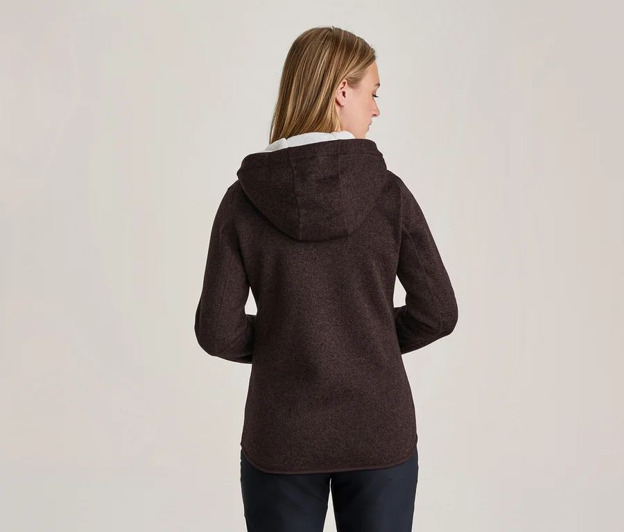 Frau von hinten gesehen, trägt eine dunkelbraune Kapuzen-Fleecejacke und dunkle Hose. Ihr blondes Haar ist sichtbar.