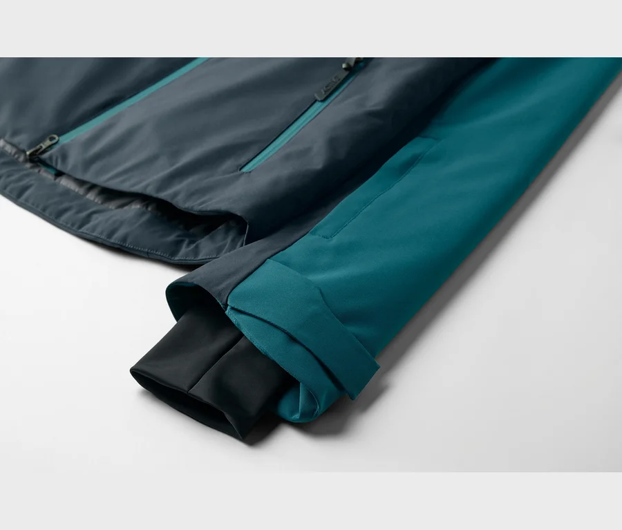 Nahaufnahme einer zweifarbigen Jacke mit dunkelblauem Rumpf und türkisfarbenem Ärmel mit schwarzem Innenbündchen, flach liegend.