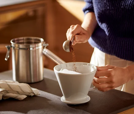 Frau schüttet Kaffee in einen weißen Kaffee Handfilter Gr. 4 mit Kaffeefilterpapier Gr. 4.