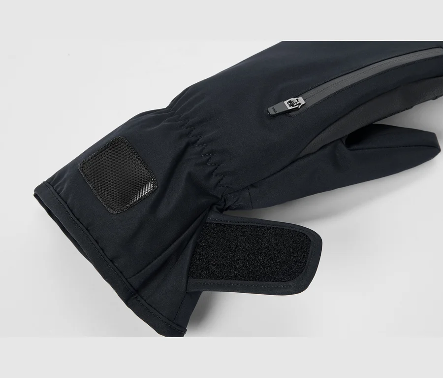 Nahaufnahme eines schwarzen Winterfäustlings mit einer Reißverschlusstasche am Handrücken, einem verstellbaren Klettverschluss am Handgelenk und einem elastischen Bündchen mit einem schwarzen strukturierten Aufnäher.
