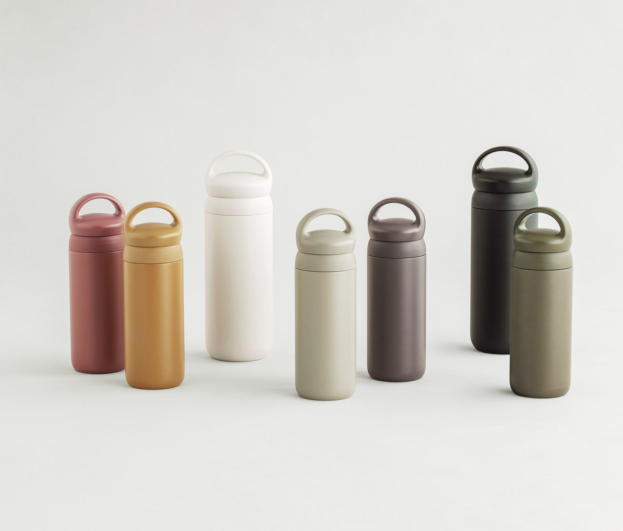 Sieben KINTO Day Off Tumbler in verschiedenen Farben: rosa, senfgelb, weiß, beige, dunkelbraun, dunkelgrau und olivgrün.