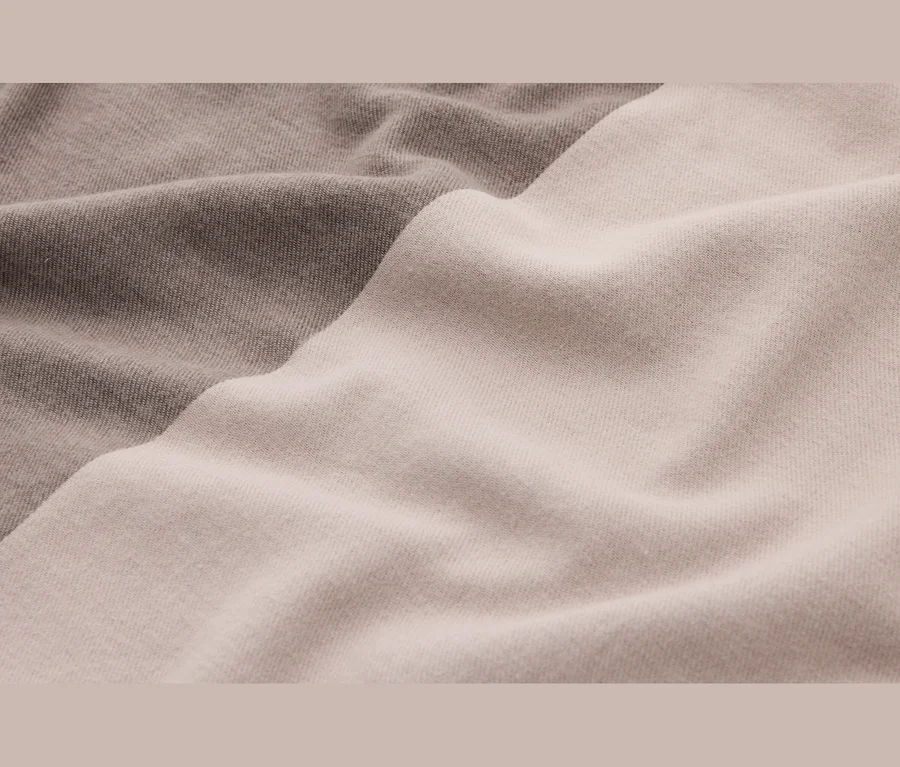 Nahaufnahme eines weichen, zweifarbigen Strickstoffs mit sanften Falten in Hellbeige und Hellbraun.