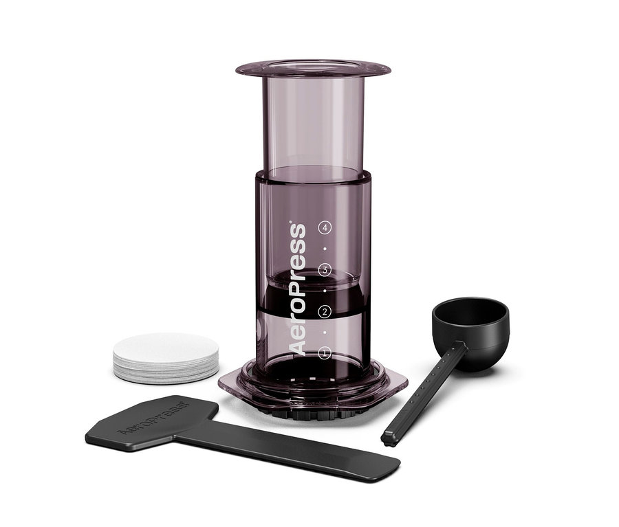 Nahaufnahme eines Aeropress Kaffeebereiters mit Zubehör, inklusive Kaffeelöffel, Rührstab und Papierfilter.