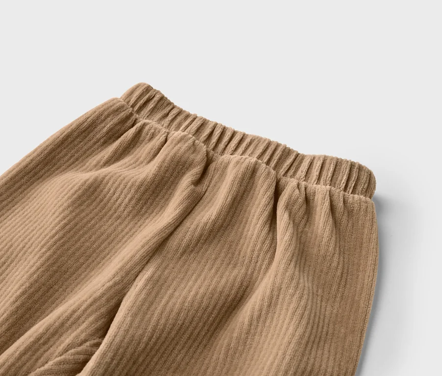 Nahaufnahme einer beigefarbenen Cordhose mit Gummibund, die die gerippte Textur des Stoffes zeigt.