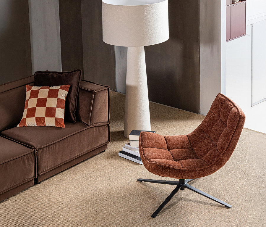 Braunes Sofa mit kariertem Kissen, daneben ein WOOOD Drehsessel "Maudi" in Braun und eine weiße Stehlampe auf beigem Teppich.