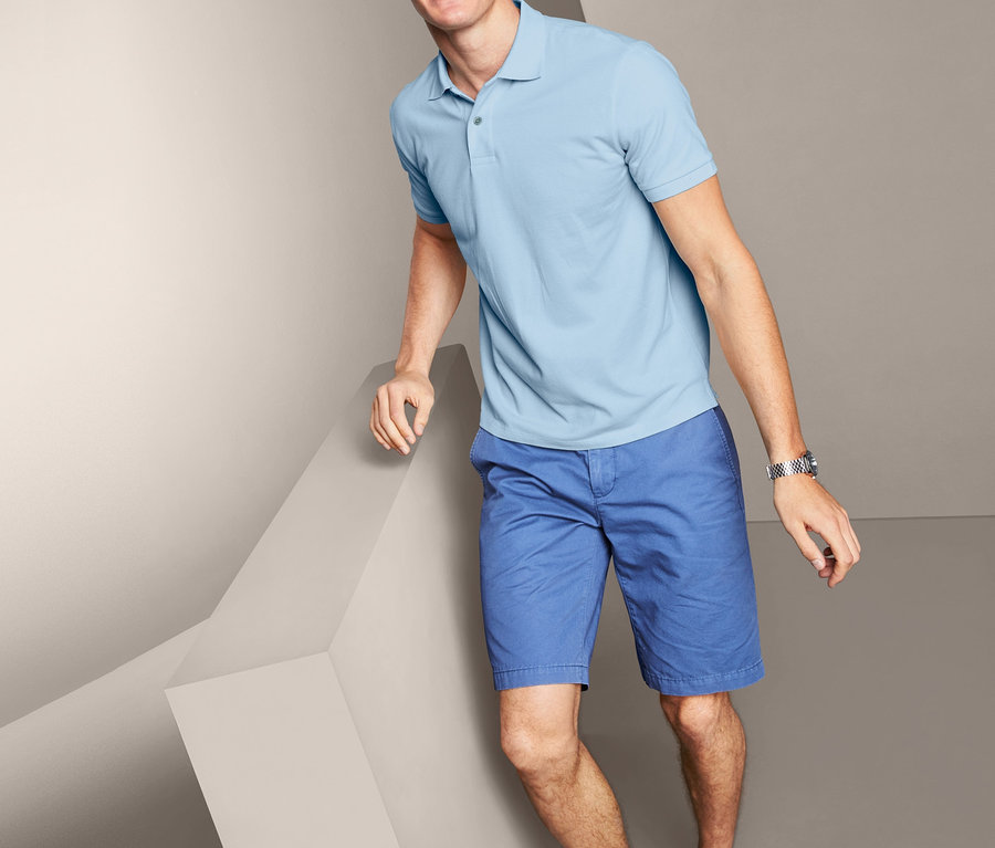 Mann posiert in Piqué-Poloshirt, blauen Shorts und Turnschuhen.