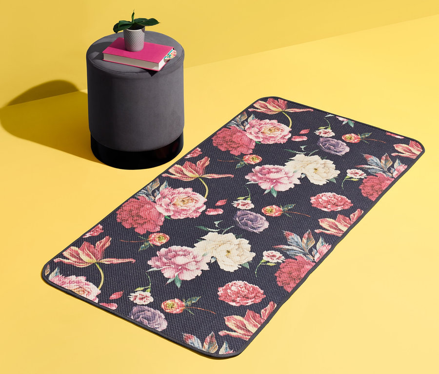 Ein Teppich, ca. 140 x 70 cm, mit Blumenmuster liegt auf gelbem Grund. Daneben steht ein grauer Hocker mit Büchern und einer Pflanze.