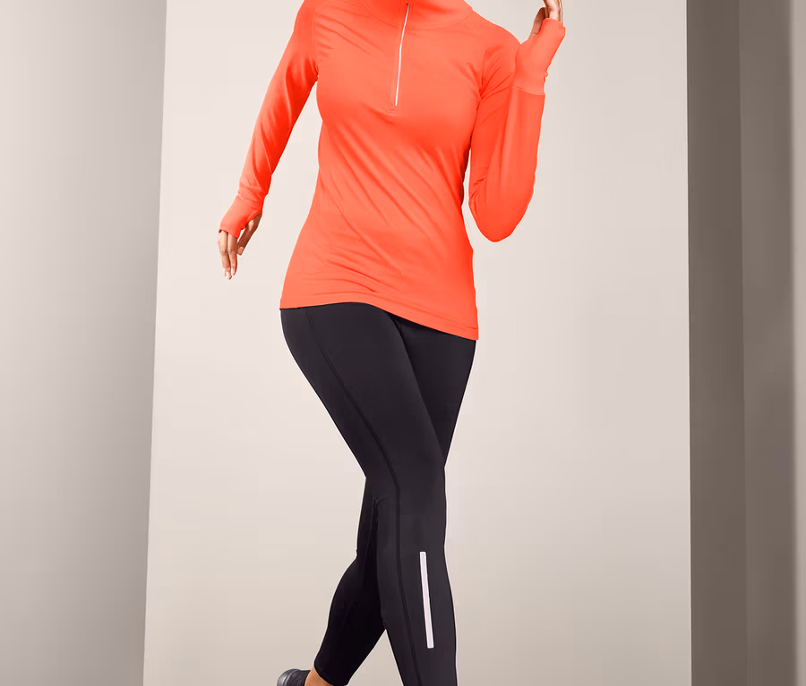 Frau posiert in neonorangefarbenem Thermo-Funktionsshirt und schwarzen Leggings.