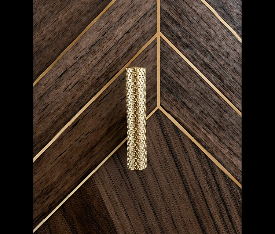 Goldener, zylindrischer Haken des Hakenpaneels #Glenn# mit Textur, auf dunklem Holzpaneel mit goldenen Chevron-Mustern.