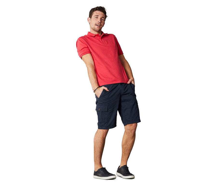 Mann posiert in rotem Poloshirt und Cargo-Shorts.