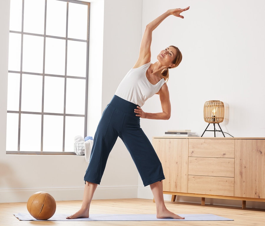 Frau dehnt sich auf einer Yogamatte und trägt eine 3/4-Sporthose.