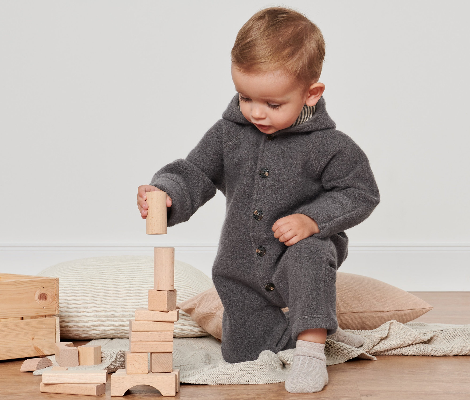 Ein Kind spielt mit Holzklötzen und trägt einen grauen Walkoverall mit RWS-Wolle.