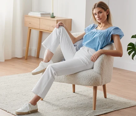 Frau sitzt im Sessel und trägt eine ausgestellte, weiße Jeans.