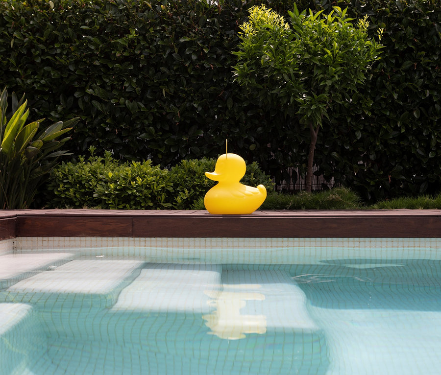 Eine gelbe Goodnight Light LED-Leuchte »Ente« S steht am Poolrand.