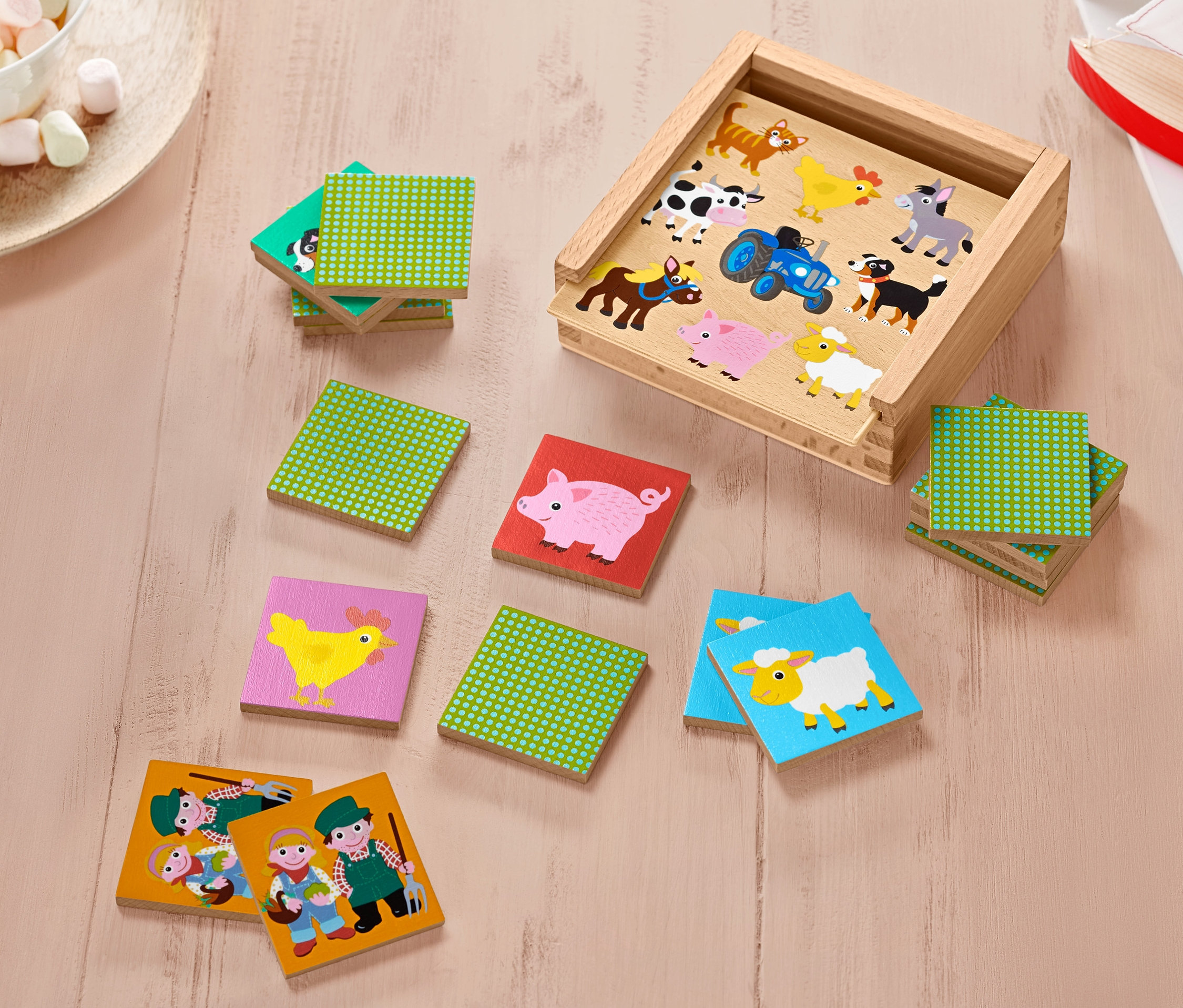 Offene Holzkiste mit Tier- und Traktormotiven und mehrere Spielsteine des Holz-Memorys. Einige Steine sind gestapelt.