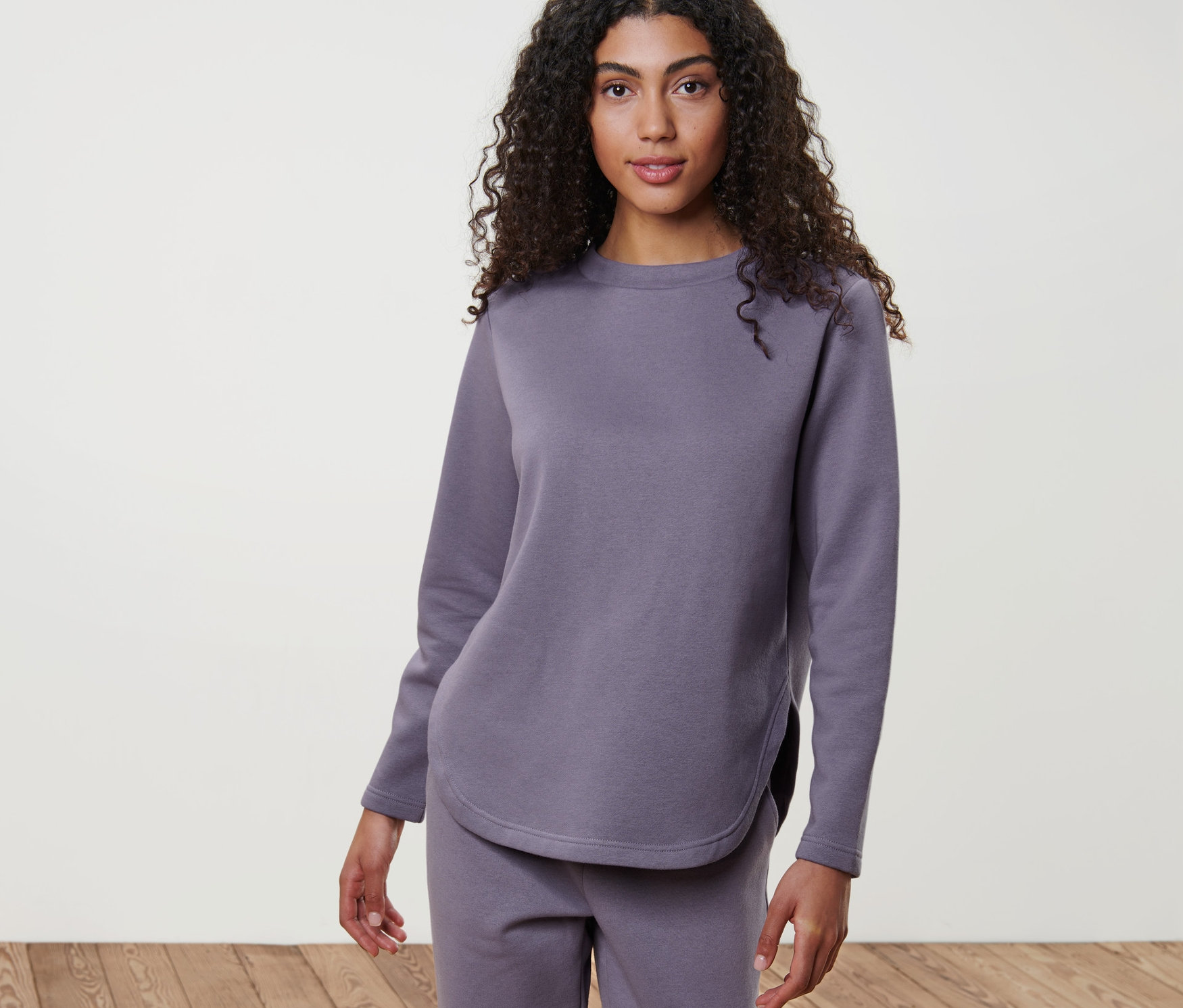 Frau in Lounge-Sweatshirt und Hose steht auf Holzboden.
