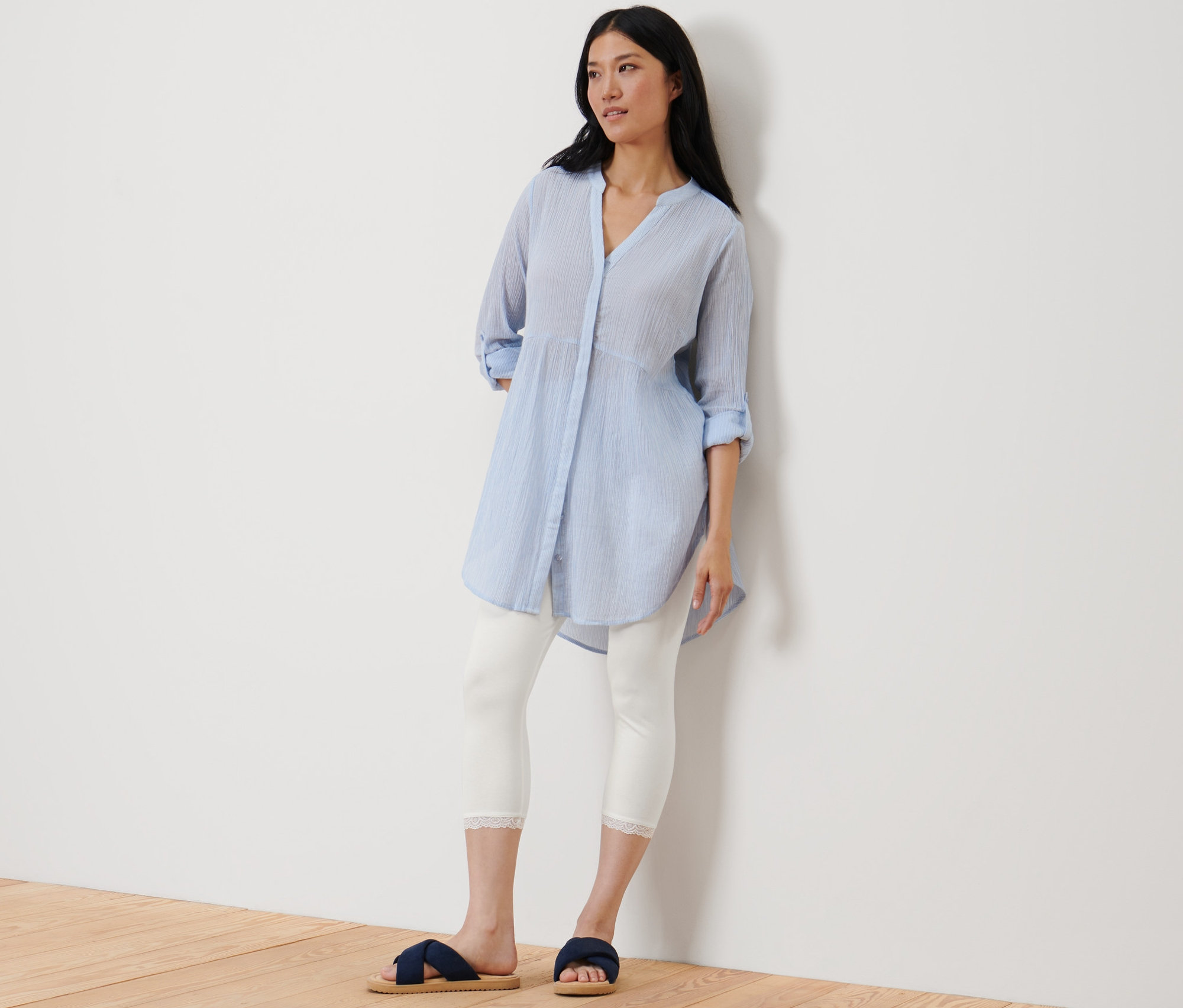 Eine Frau lehnt an einer Wand und trägt eine weiße 3/4-Leggings mit Spitzenborte.