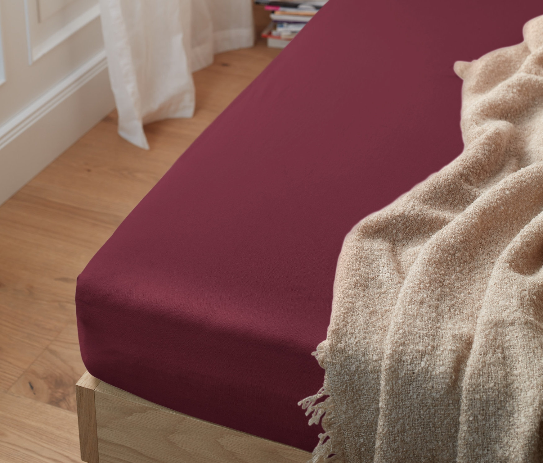 Detailansicht eines Holzbettes mit einem dunkelroten Jersey-Spannbettlaken.